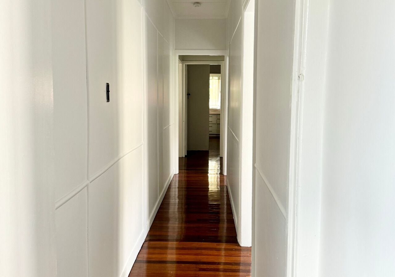 A long, narrow hallway with white walls and wooden flooring.