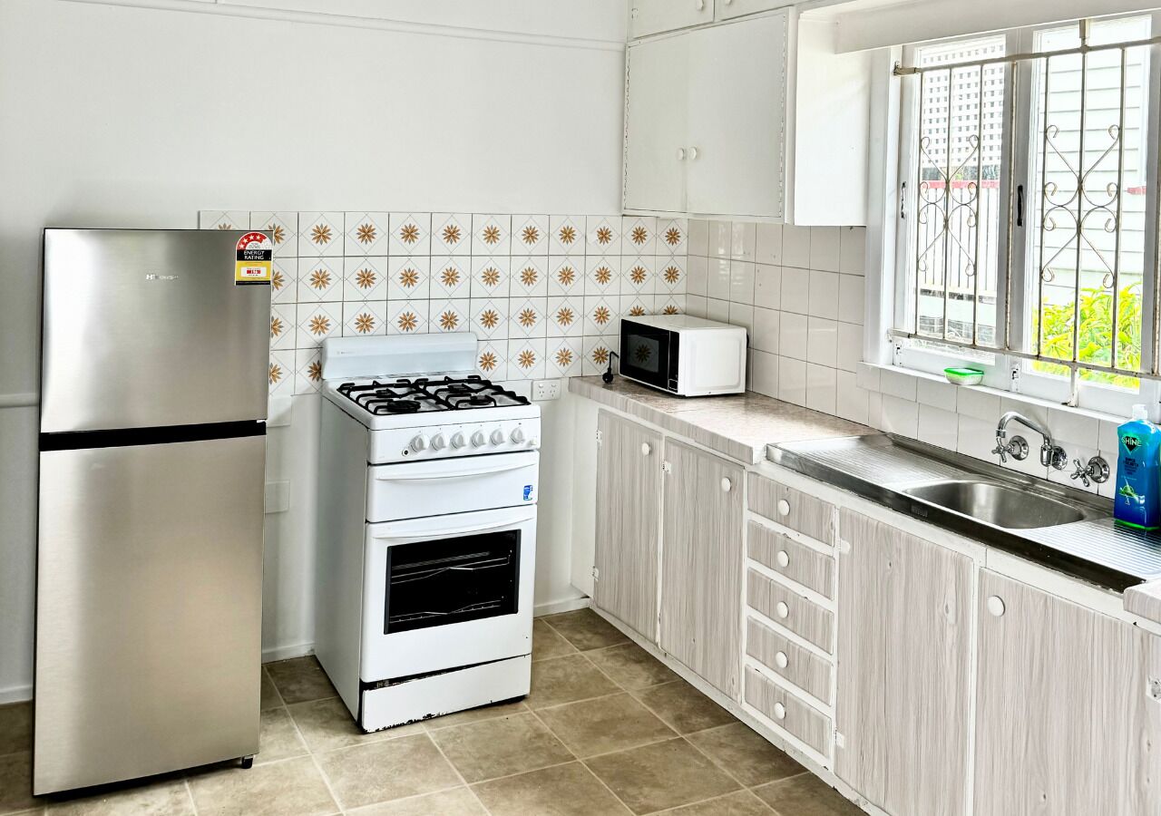 A compact kitchen with a stainless steel refrigerator, a gas stove, a microwave, and a sink with a window above.