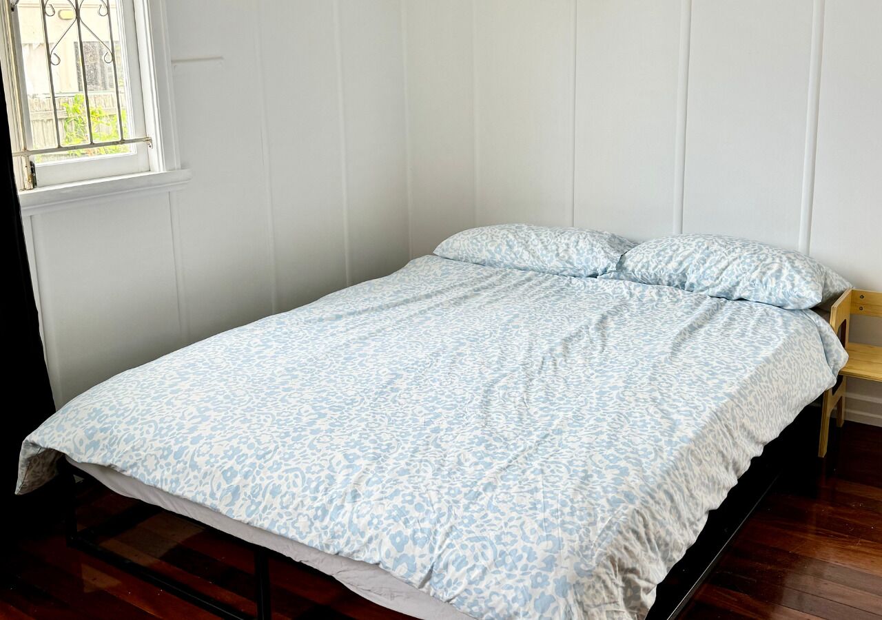 Un lit simple avec une couvre-lit à motifs, dans une pièce aux murs blancs et au plancher en bois.