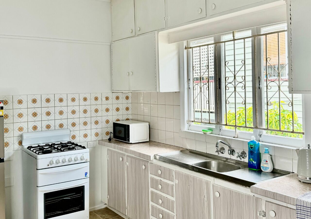 A kitchen with white cabinets, a gas stove, a microwave, and a window with a view of greenery.