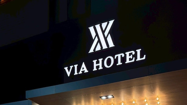 El exterior del Via Hotel, con un diseño moderno, que destaca su logotipo, una entrada bien iluminada y un frente de vidrio.