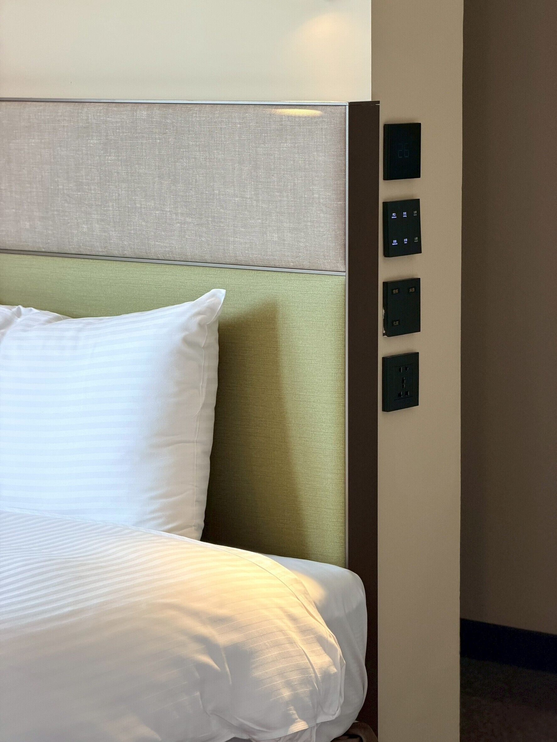 Una habitación de hotel con una cama, cabecera y panel de control fijado a la pared.