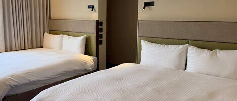 A hotel room with two beds, a headboard, a door, and a light switch on the wall.