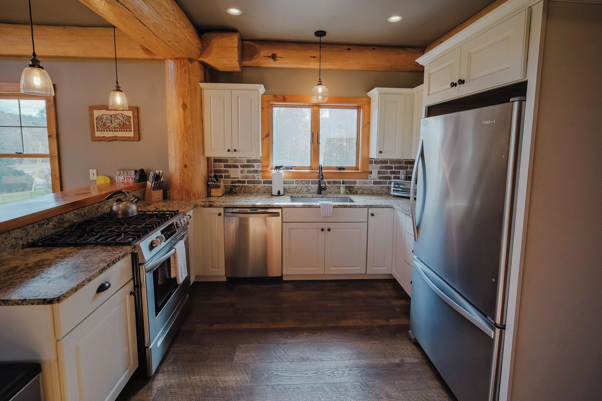 A kitchen with white cabinets, a stainless steel refrigerator, a granite countertop, and a window with a view.