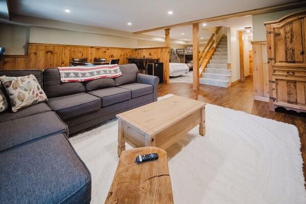 Un salon chaleureux avec un canapé d’angle gris, une table basse en bois et un tapis à poils longs blanc.