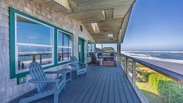 A wooden deck with Adirondack chairs and a table, overlooking a beach and ocean.