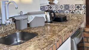Uma cozinha com bancada de granito, pia de aço inoxidável, chaleira e escorredor de louça.