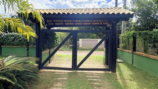 Uma área externa coberta com telhado de azulejos, rodeada por vegetação e céu claro.