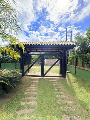 A covered outdoor area with a tiled roof, surrounded by greenery and a clear sky. - Beach House Rosa/Ibiraquera (Imbituba)
