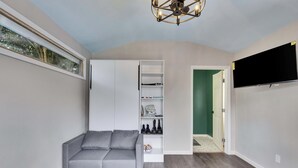 Een moderne woonkamer met een grijze hoekbank, een wit wandrek, een flatscreen televisie en een plafondlamp.