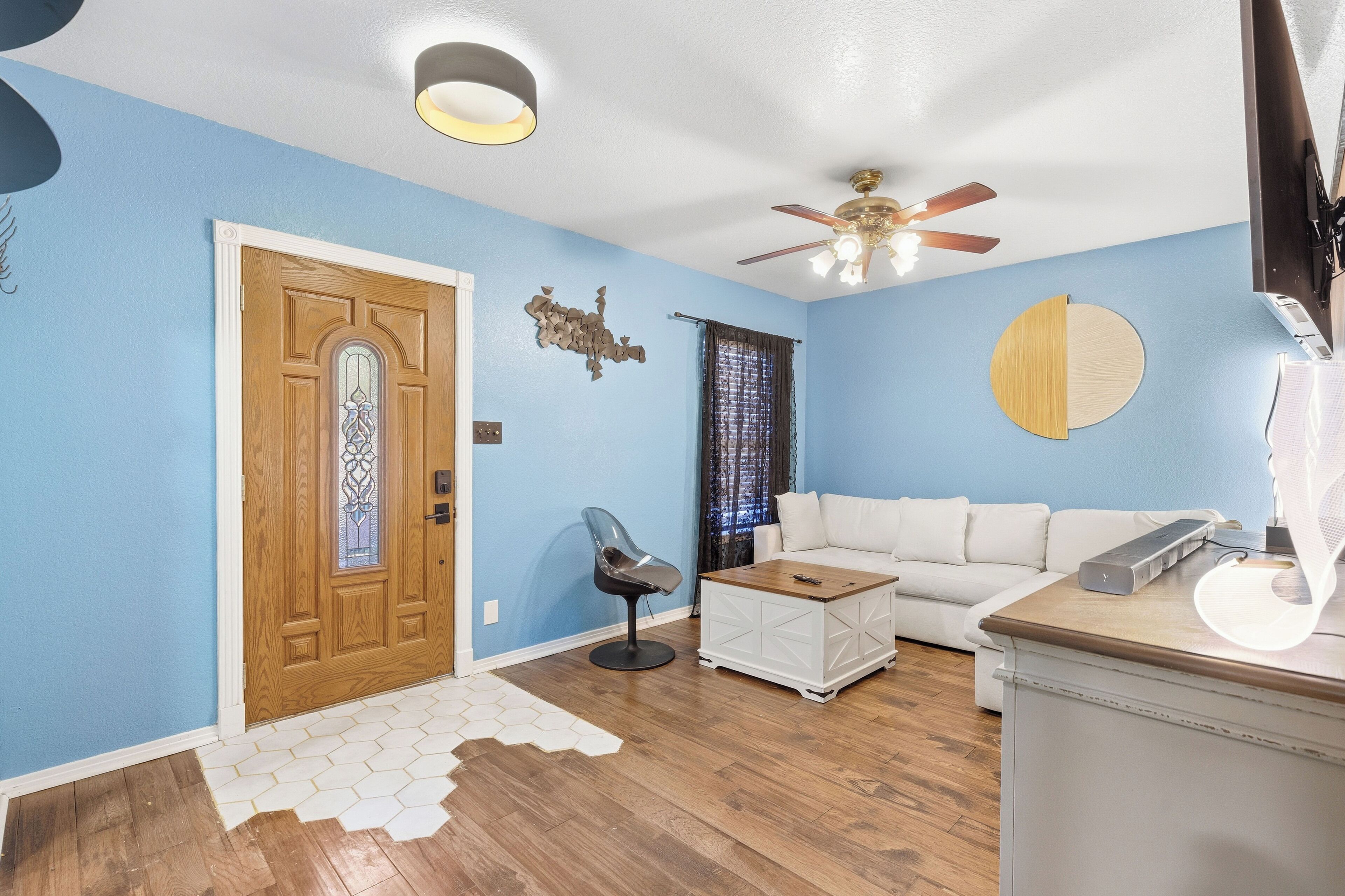 A living room with a wooden door, a white sofa, a coffee table, and a ceiling fan.