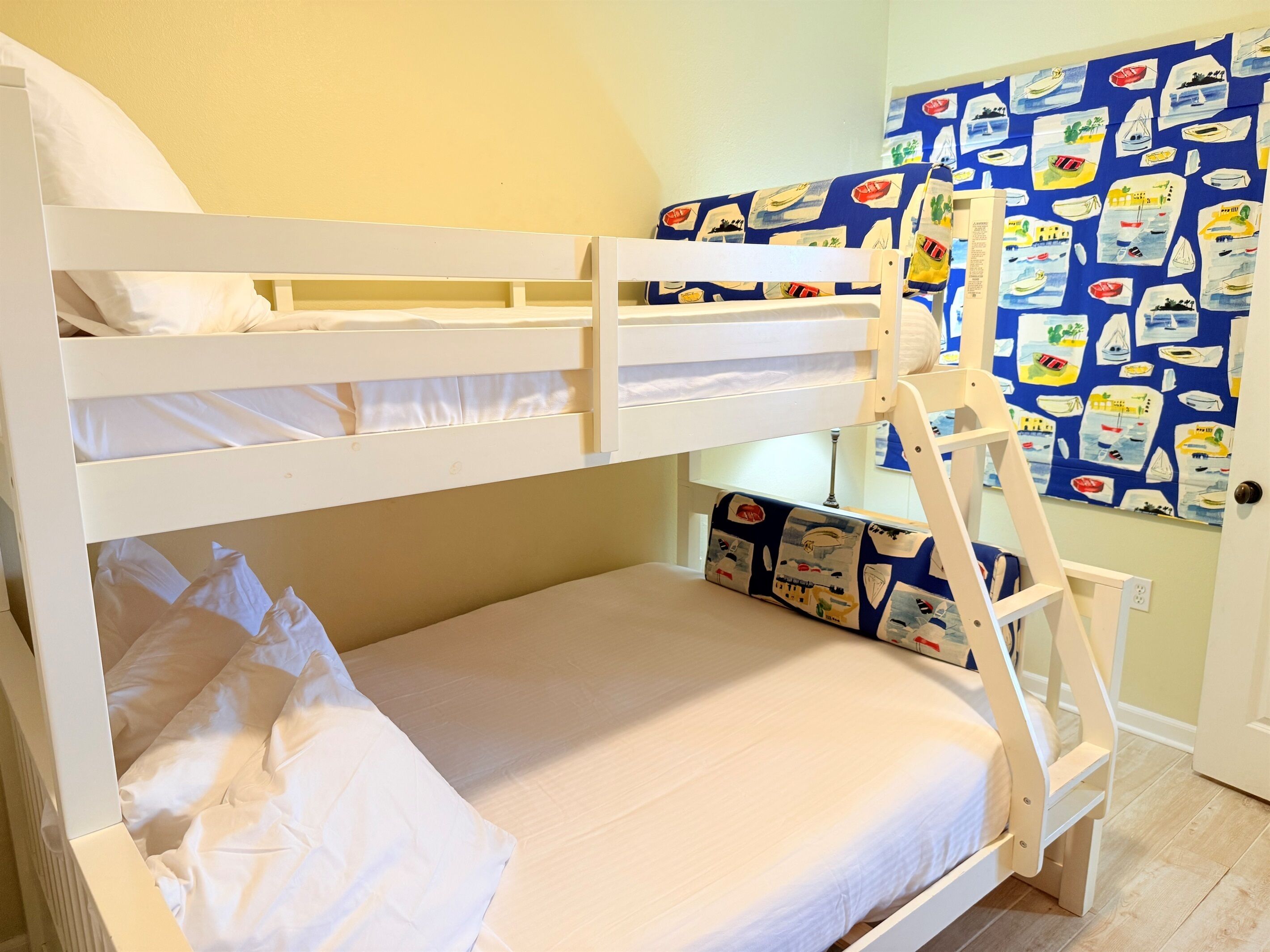 A bunk bed with a ladder, white bedding, and a wall with nautical-themed artwork.