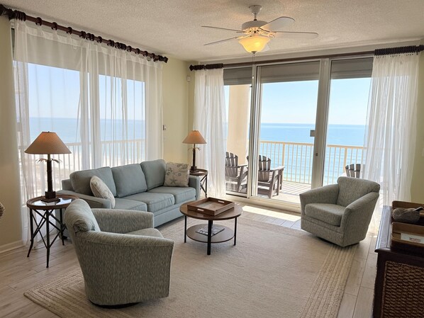 A spacious living area with a sofa, armchairs, a coffee table, and a balcony with a view of the ocean.
