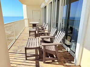 A balcony with wooden chairs and a table, overlooking the ocean.