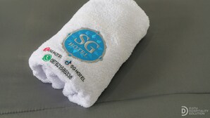 Une serviette blanche ornée du logo de l’hôtel SG et de ses coordonnées.