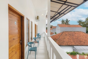 A balcony with wooden doors, a row of blue chairs, and a view of a residential area with red-tiled roofs.