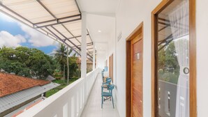 Un balcon avec un sol carrelé, une rangée de chaises bleues et une porte en bois.
