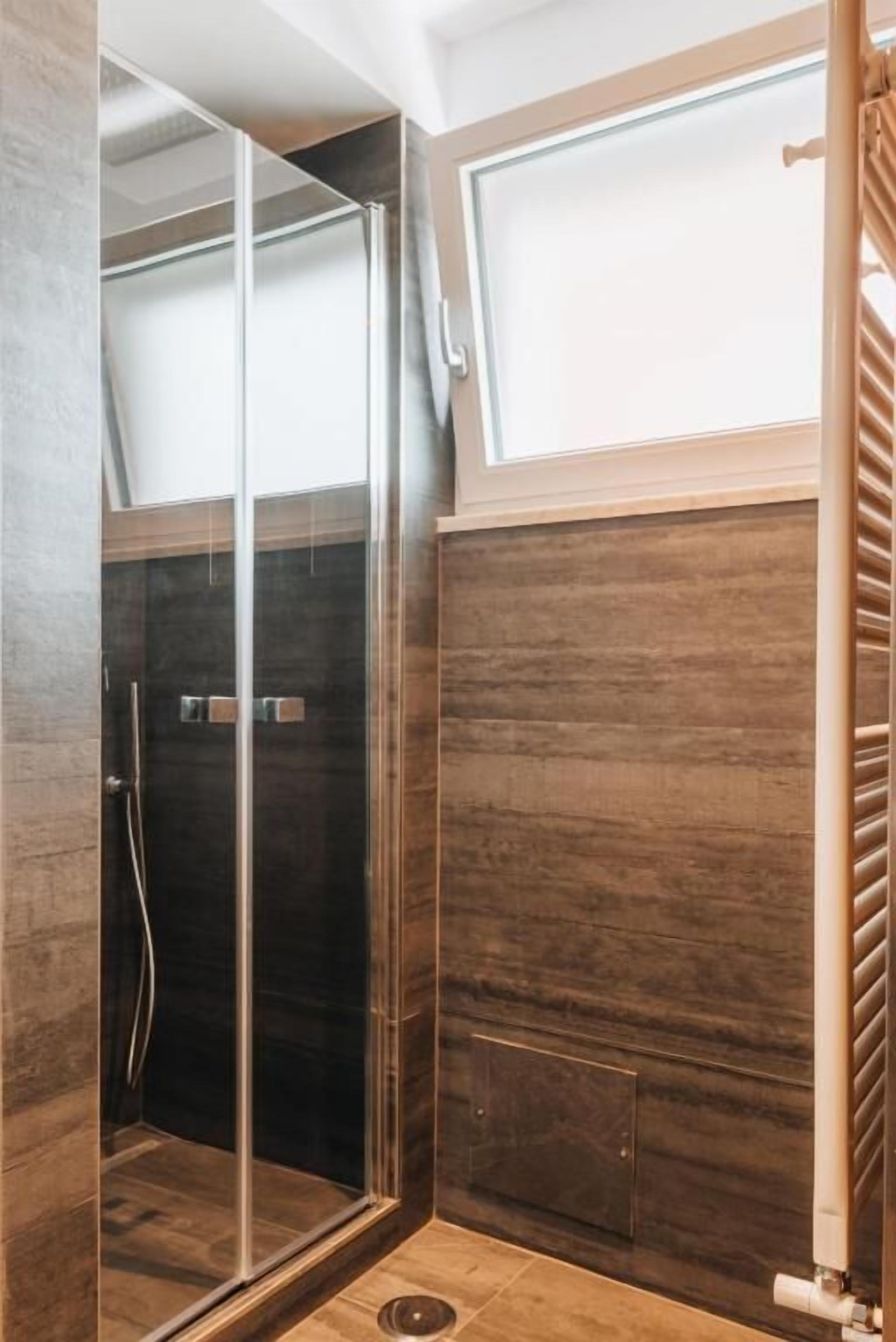 A modern shower with glass doors, a wooden panel wall, and a visible showerhead.