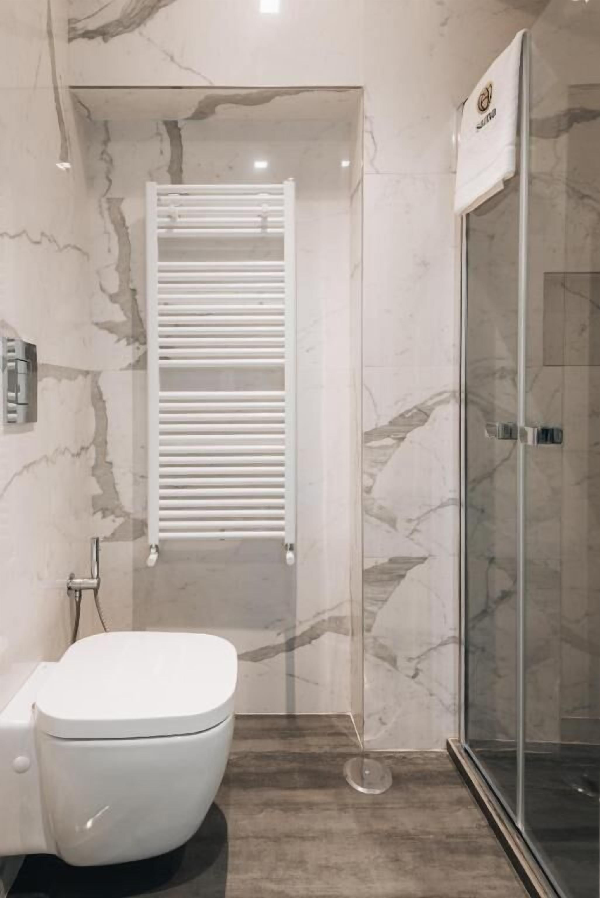 A modern bathroom with a white toilet, a glass shower enclosure, and a marble-tiled wall.