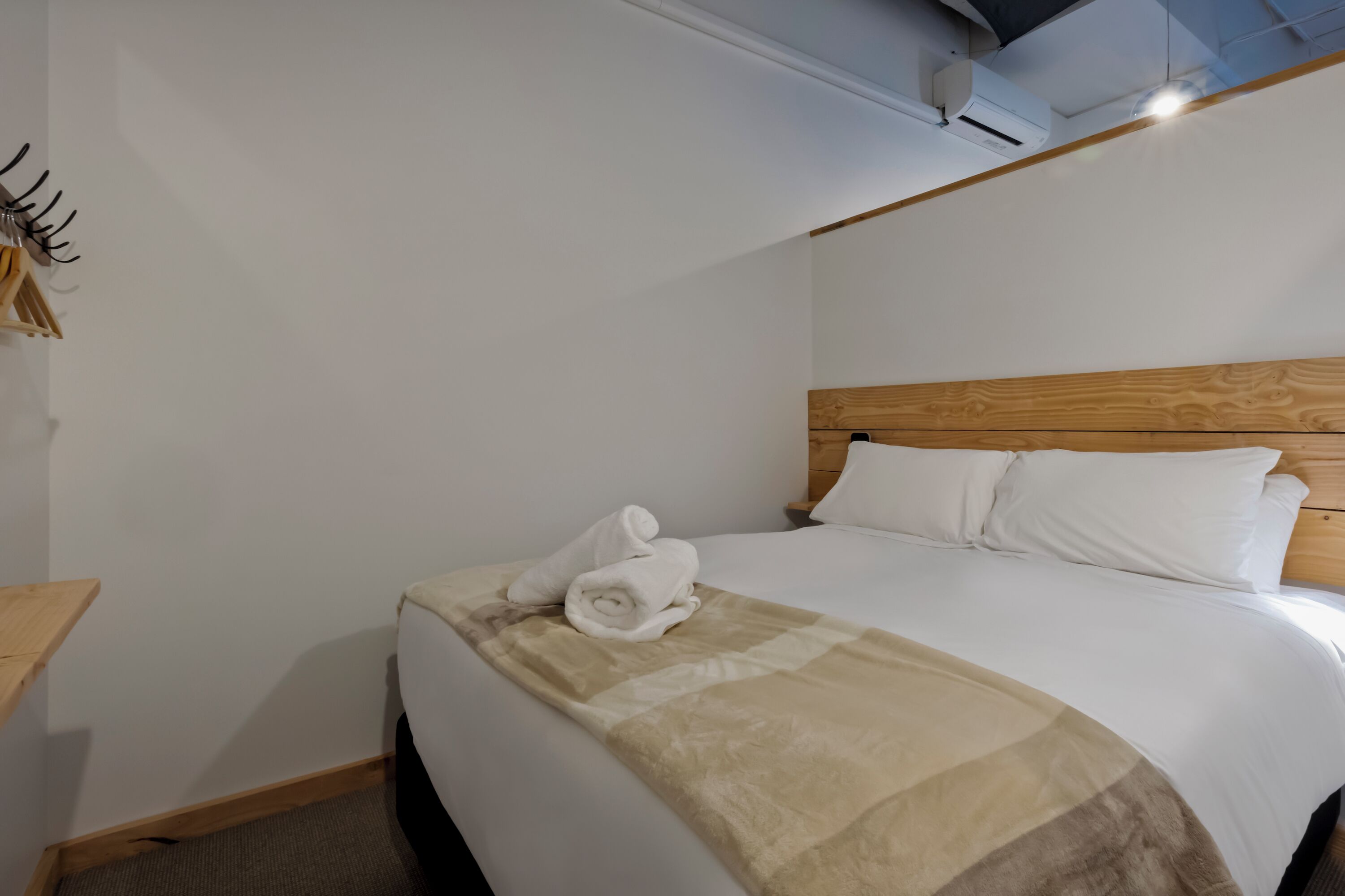 A hotel room with a wooden headboard, a neatly made bed with white linens, and a beige throw blanket.