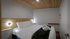 A neatly made bed with white linens, a green throw blanket, and a rolled towel on the side. - Central Lofts 4 & 5 - Accessible - Brand New! (Queenstown)