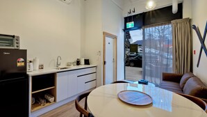 A modern kitchen with a refrigerator, sink, and countertop. There is a dining area with a table and chairs. A window with a view of cars outside is visible. - Central Lofts 4 & 5 - Accessible - Brand New! (Queenstown)