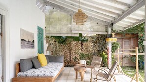 A covered outdoor seating area with a wooden bench, a rattan chair, and a small table. - Villa Zen Bingin (Pecatu)