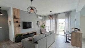 Uma sala de estar moderna com um sofá cinzento, uma televisão e luminárias pendentes.