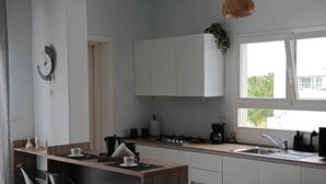 Uma cozinha moderna com armários brancos, fogão a gás, cafeteira e janela com vista para o verde.