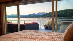 A bedroom with a large bed, a balcony with a view of a lake and mountains, and a sliding glass door. - Hood Canal Resort in Union, WA (Union)
