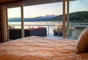 Una camera da letto con un letto grande, un balcone vista lago e montagne, e una porta scorrevole in vetro.