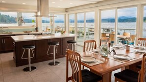 A modern kitchen with a large island, bar stools, and a dining area with a view of a lake. - Hood Canal Resort in Union, WA (Union)