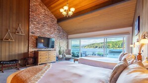 A spacious bedroom with a large bed, a TV, and a view of a lake. - Walls of Glass (Union)