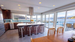 A modern kitchen with a large island, bar stools, and a view of the sea. - Walls of Glass (Union)