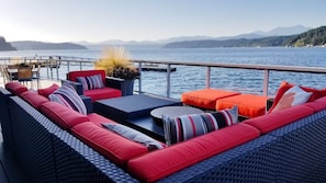 Una terraza con mobiliario de mimbre, una mesa y vistas al lago y las montañas.