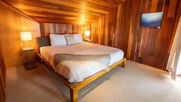 A wooden-paneled bedroom with a large bed, two bedside lamps, and a painting on the wall.