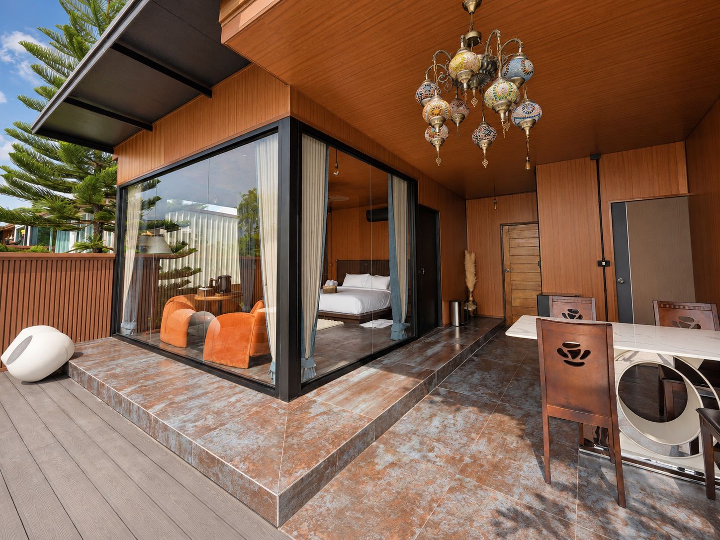 A modern outdoor living area with a glass enclosure, wooden deck, and a dining setup.
