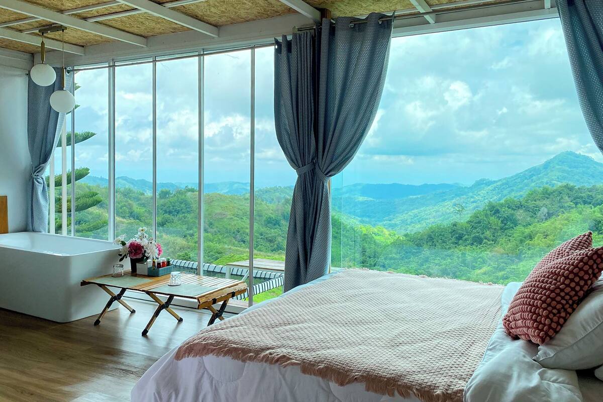 Ein Schlafzimmer mit großem Fenster, einem Bett, einem Tisch und einer Badewanne.