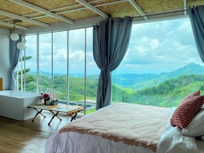 A bedroom with a large window, a bed, a table, and a bathtub. - Area21 Khaokho (Khao Kho)