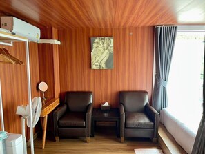 A room with wooden panel walls, two leather chairs, a small table with a mirror, a fan, and a painting.