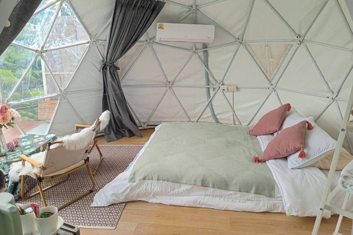 Ein gemütliches Zimmer mit Bett, Kissen, einem Sessel und einem Tisch mit Tasse und Untertasse.