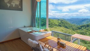 A modern bathroom with a large bathtub, wooden flooring, and a view of lush green mountains through large windows. - Area21 Khaokho (Khao Kho)