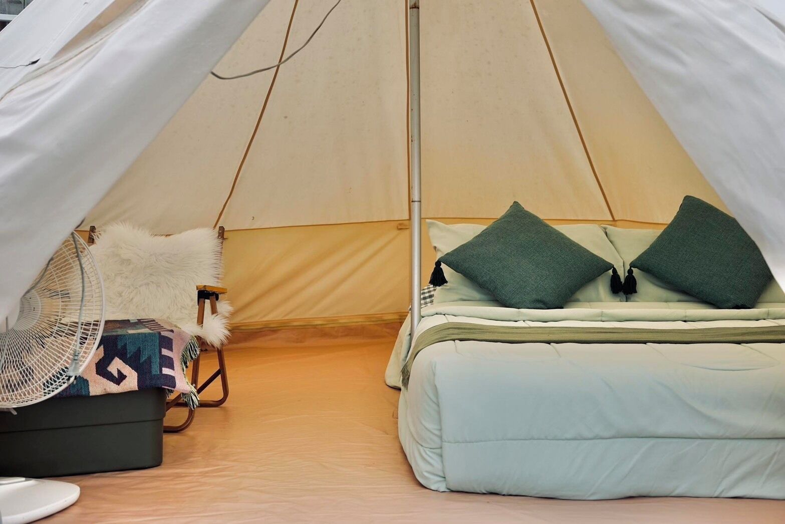 A tent with a bed, a fan, and a suitcase.