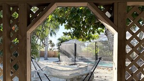 A hammock under a wooden pergola with a pool and a covered area in the background. - Englewood Escape – Pet Friendly + Heated Pool (Englewood)
