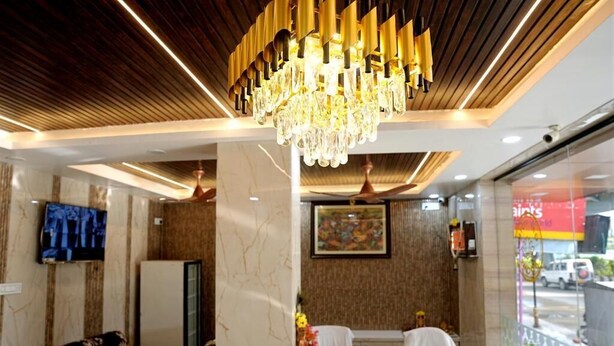 Uma área de recepção de hotel com um balcão de mármore, um candelabro, um sofá, uma televisão e um quadro na parede.