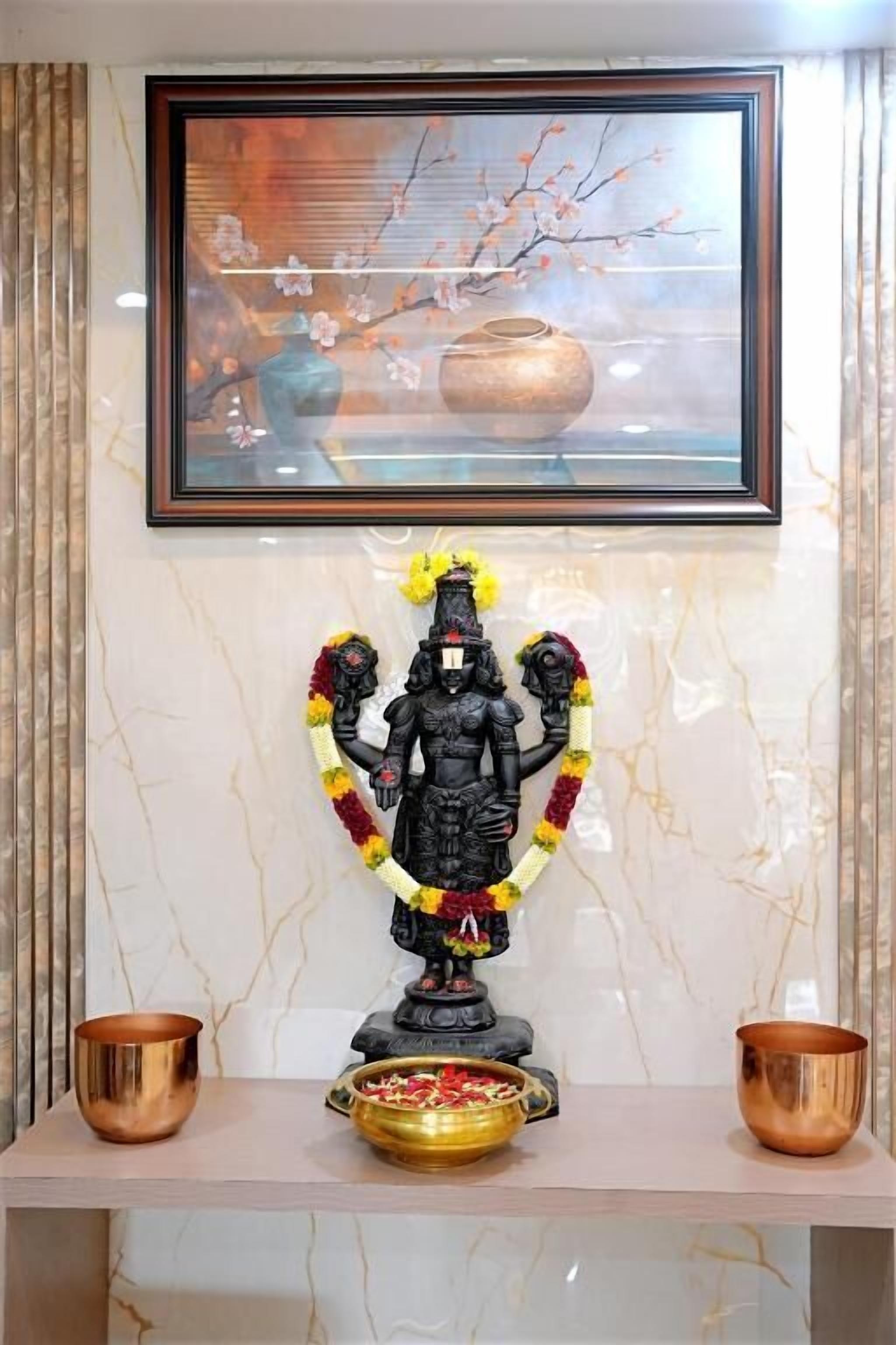 A statue with a garland, two copper bowls, and a framed painting on a marble wall.