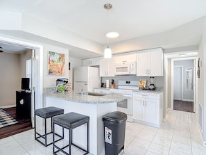 A modern kitchen with white cabinets, a granite countertop, and a central island with bar stools.