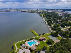 An aerial view of a residential area with a large body of water, a dock, and a swimming pool.
