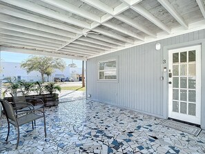A covered patio with a tiled floor, a bench, and a door with a number plate.