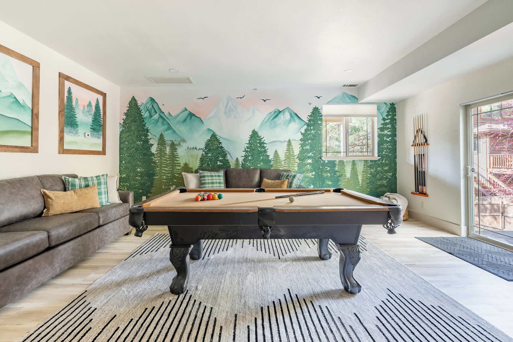 A pool table in a living room with a mural of mountains and trees on the wall.